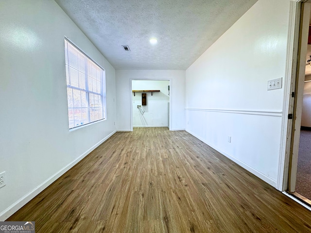 unfurnished living room with visible vents, a textured ceiling, baseboards, and wood finished floors