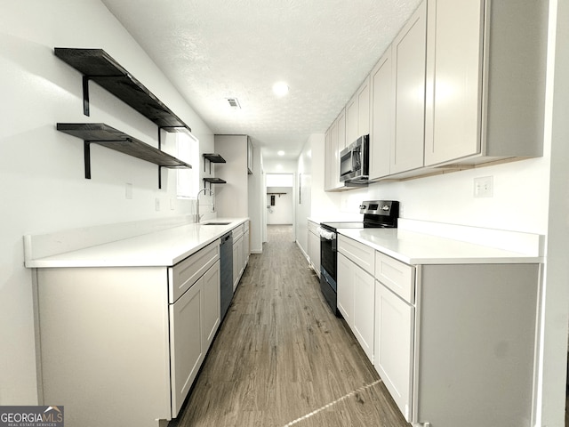 kitchen featuring open shelves, stainless steel appliances, a sink, a textured ceiling, and light wood-type flooring