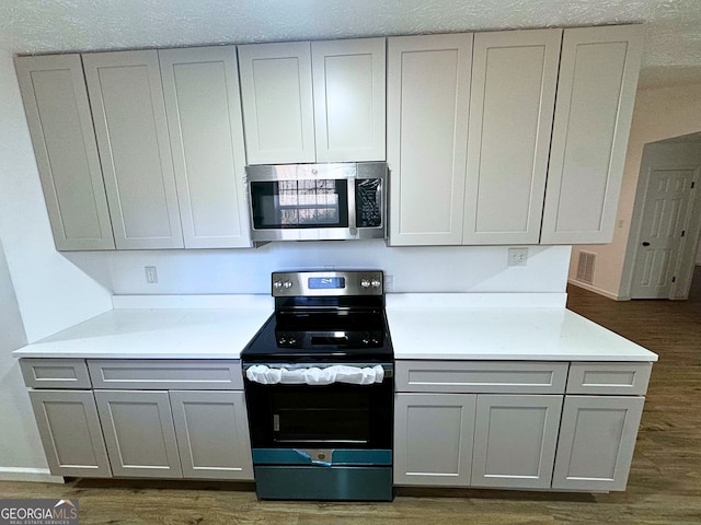 kitchen with gray cabinetry, stainless steel appliances, baseboards, light countertops, and dark wood-style floors