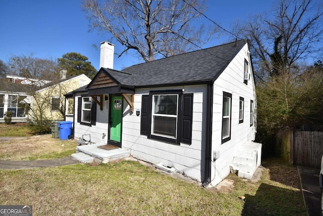 bungalow-style home featuring roof with shingles, fence, a chimney, and a front lawn