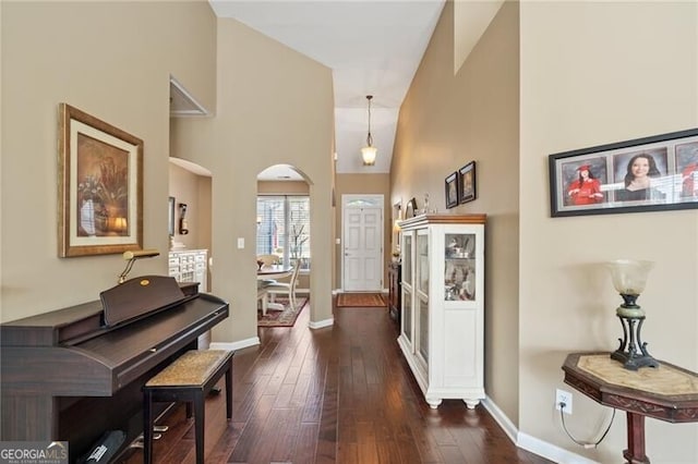 interior space featuring dark wood-style floors, arched walkways, a towering ceiling, and baseboards