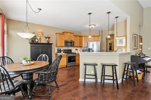 kitchen featuring dark wood finished floors, decorative backsplash, appliances with stainless steel finishes, a peninsula, and a kitchen breakfast bar