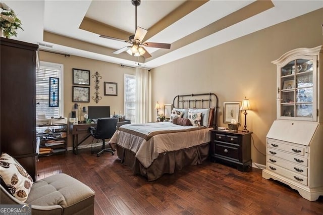 bedroom featuring dark wood-style floors, ceiling fan, multiple windows, and a raised ceiling