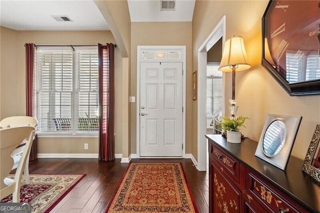 entrance foyer featuring arched walkways, dark wood-style flooring, visible vents, and baseboards