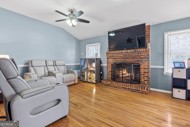 living room with baseboards, lofted ceiling, ceiling fan, wood finished floors, and a brick fireplace