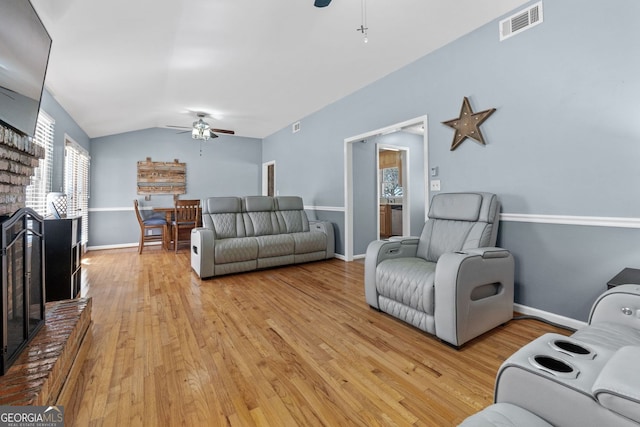 living room with visible vents, a ceiling fan, a brick fireplace, vaulted ceiling, and light wood-type flooring