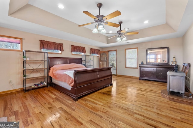 bedroom with baseboards, a ceiling fan, a tray ceiling, light wood-style floors, and recessed lighting