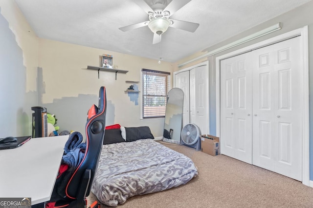 carpeted bedroom featuring multiple closets, a textured ceiling, and a ceiling fan