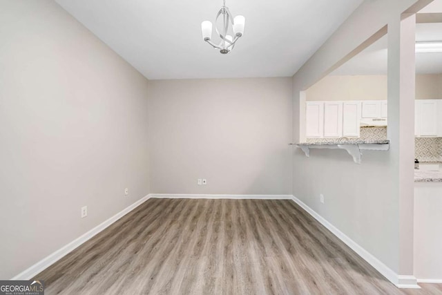 unfurnished dining area with light wood finished floors, an inviting chandelier, and baseboards