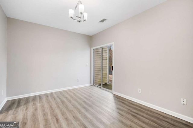 spare room featuring an inviting chandelier, baseboards, visible vents, and wood finished floors