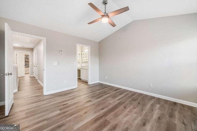 unfurnished bedroom featuring baseboards, a ceiling fan, lofted ceiling, light wood-style flooring, and ensuite bathroom