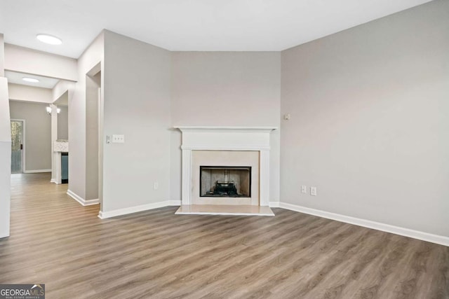 unfurnished living room featuring a fireplace with raised hearth, baseboards, and wood finished floors