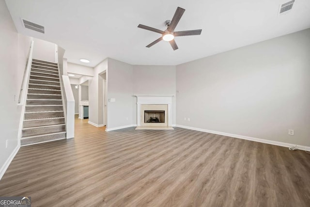 unfurnished living room with a fireplace with flush hearth, stairs, visible vents, and wood finished floors