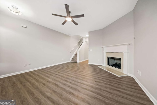 unfurnished living room with a fireplace with raised hearth, stairway, wood finished floors, and baseboards