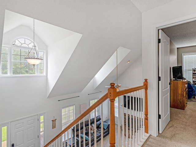 hallway featuring light carpet, high vaulted ceiling, an upstairs landing, and a wealth of natural light