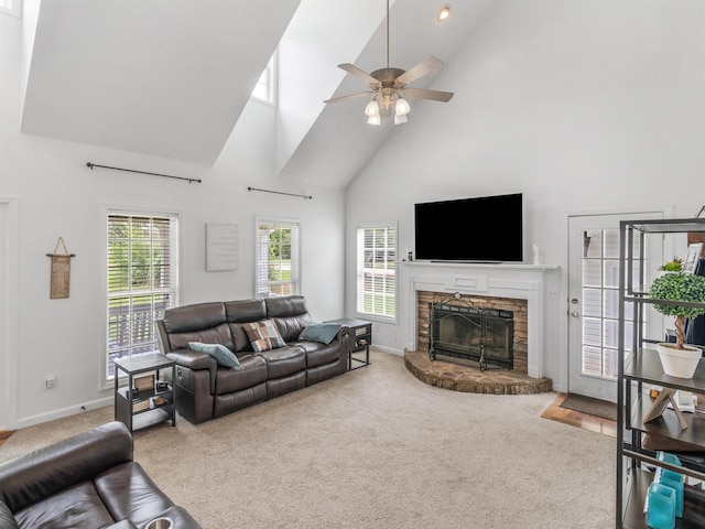 carpeted living room featuring ceiling fan, high vaulted ceiling, a stone fireplace, and baseboards