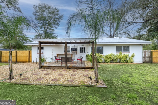 rear view of property with a deck, metal roof, fence, a lawn, and stucco siding