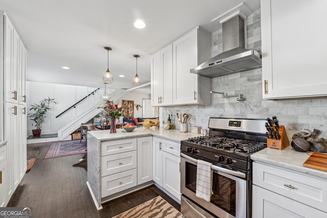 kitchen with a peninsula, white cabinetry, wall chimney range hood, decorative backsplash, and stainless steel gas stove