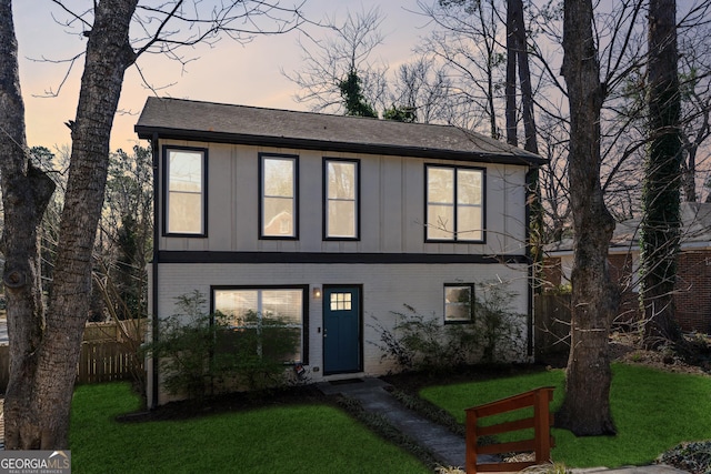 view of front of property with board and batten siding, brick siding, fence, and a front lawn