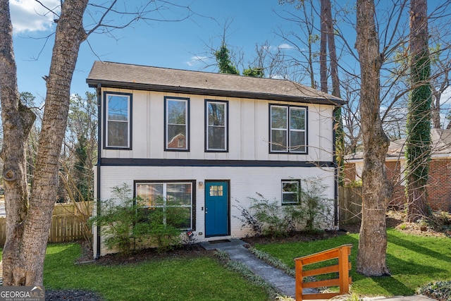 view of front facade featuring board and batten siding, brick siding, fence, and a front lawn