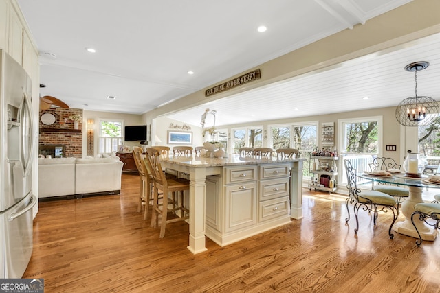 kitchen featuring light wood finished floors, a chandelier, open floor plan, a breakfast bar, and stainless steel fridge