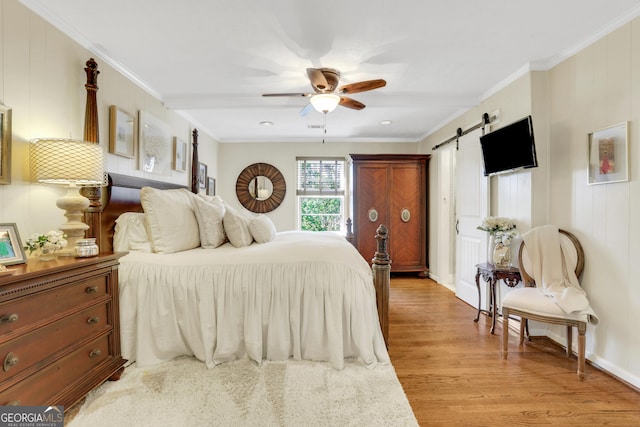 bedroom with ceiling fan, a barn door, light wood-style floors, and ornamental molding