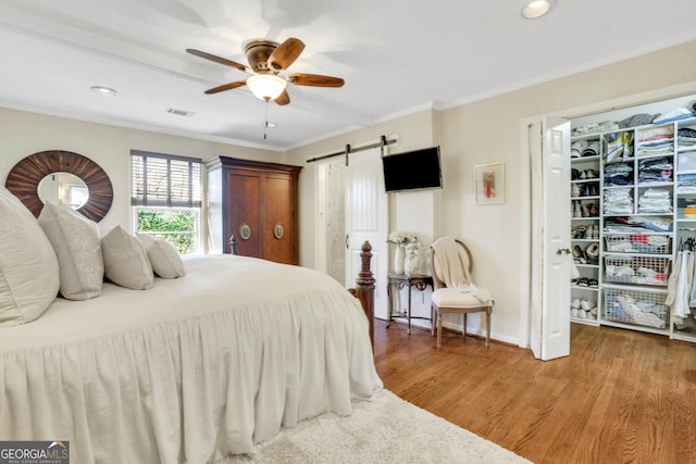 bedroom with visible vents, light wood-style flooring, ornamental molding, a barn door, and ceiling fan