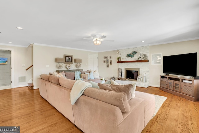 living room featuring visible vents, stairs, crown molding, a brick fireplace, and light wood-type flooring