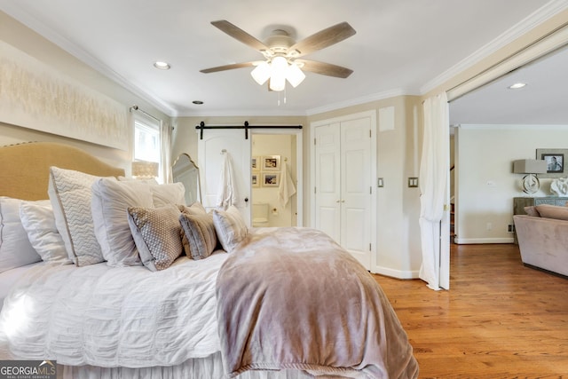 bedroom featuring baseboards, light wood-style flooring, recessed lighting, crown molding, and a barn door