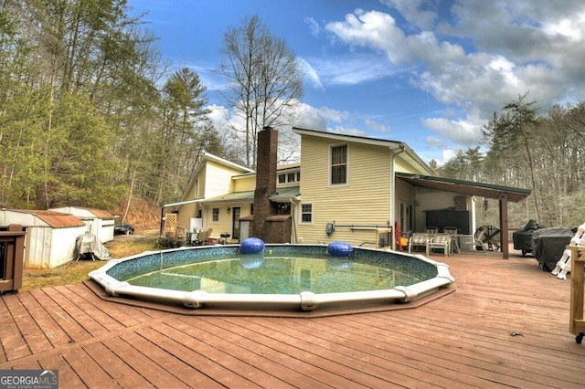 wooden terrace featuring a storage unit, an outdoor pool, and an outbuilding