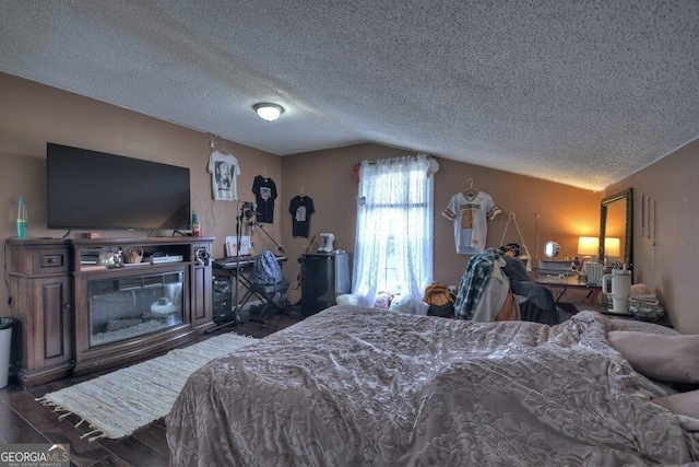 bedroom with lofted ceiling, a textured ceiling, and wood finished floors