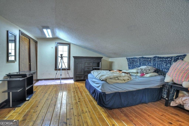 bedroom with lofted ceiling, a textured ceiling, and hardwood / wood-style floors