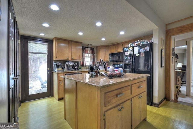 kitchen with black appliances, light wood finished floors, a textured ceiling, and a center island