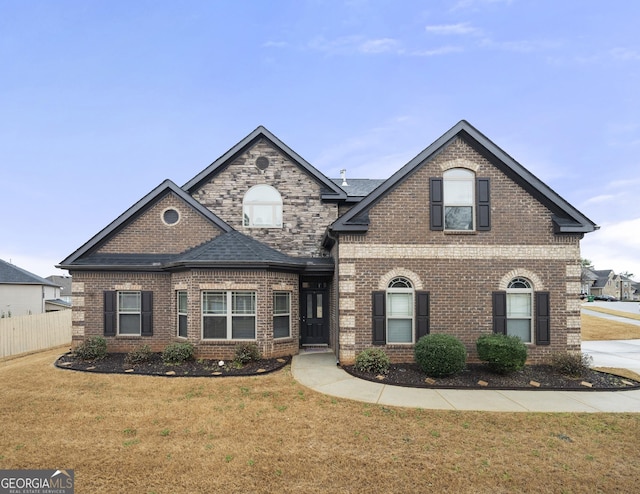 view of front of property featuring a front yard, fence, brick siding, and roof with shingles