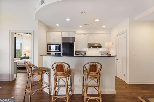 kitchen with white cabinets, dark countertops, stainless steel microwave, under cabinet range hood, and fridge