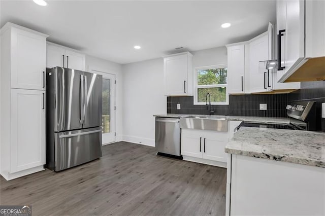 kitchen featuring stainless steel appliances, wood finished floors, a sink, white cabinetry, and decorative backsplash