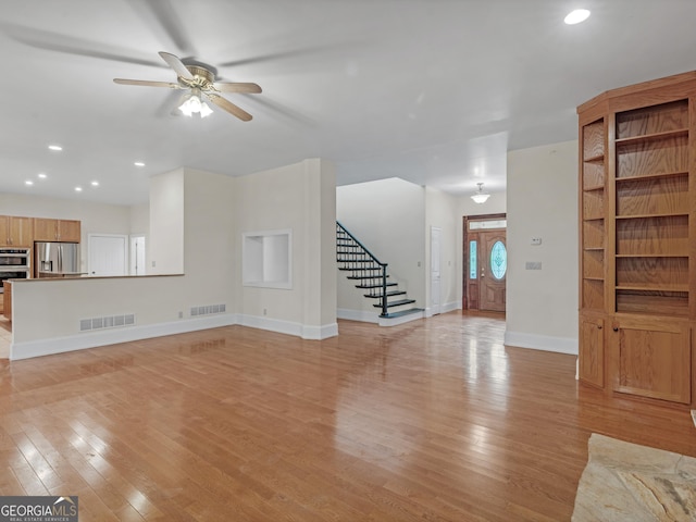 unfurnished living room featuring light wood-style flooring, stairway, and visible vents