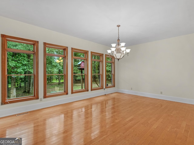 unfurnished room featuring visible vents, a notable chandelier, light wood-style flooring, and baseboards