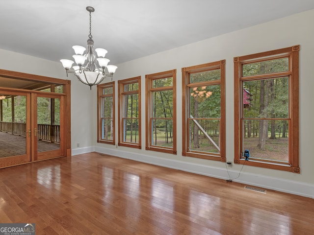 unfurnished dining area with an inviting chandelier, visible vents, baseboards, and hardwood / wood-style flooring