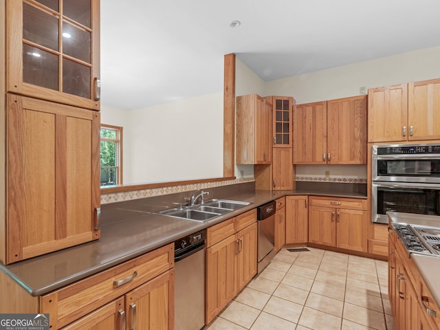 kitchen featuring light tile patterned floors, a sink, appliances with stainless steel finishes, dark countertops, and glass insert cabinets