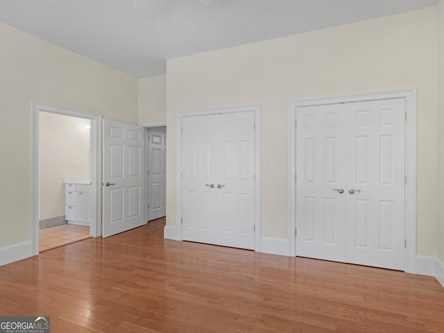 unfurnished bedroom with baseboards, multiple closets, and wood finished floors