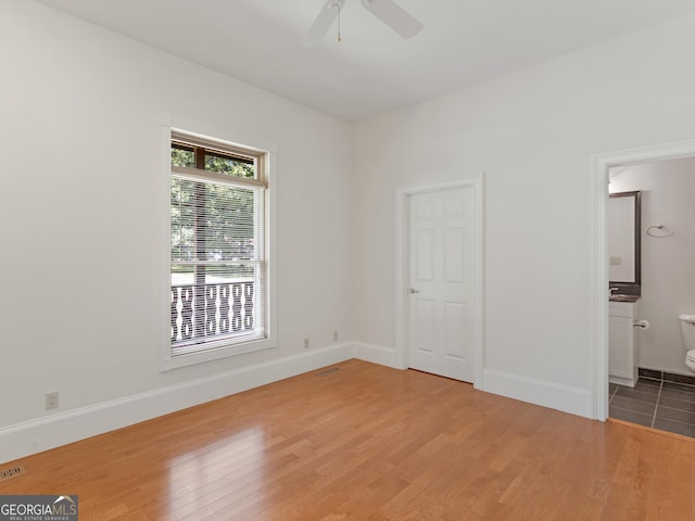 unfurnished bedroom with visible vents, a ceiling fan, ensuite bath, wood finished floors, and baseboards