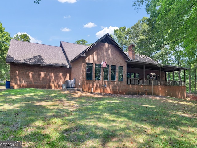 rear view of property with brick siding, a lawn, and a chimney