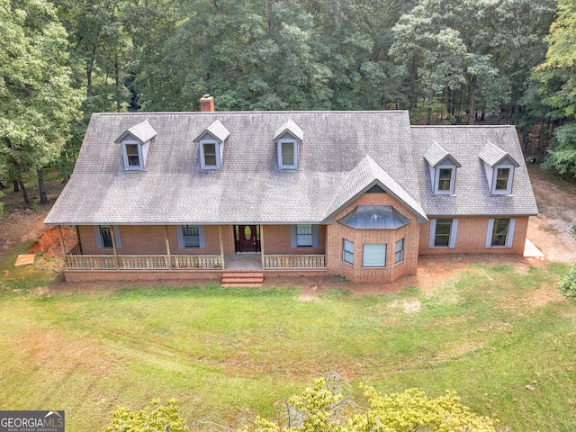 view of front of property featuring brick siding, a chimney, a porch, a shingled roof, and a front yard