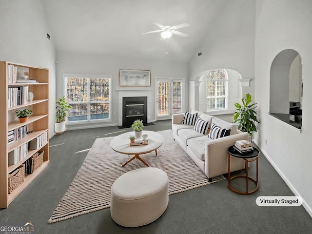 living room featuring high vaulted ceiling, carpet flooring, a fireplace with flush hearth, a ceiling fan, and baseboards