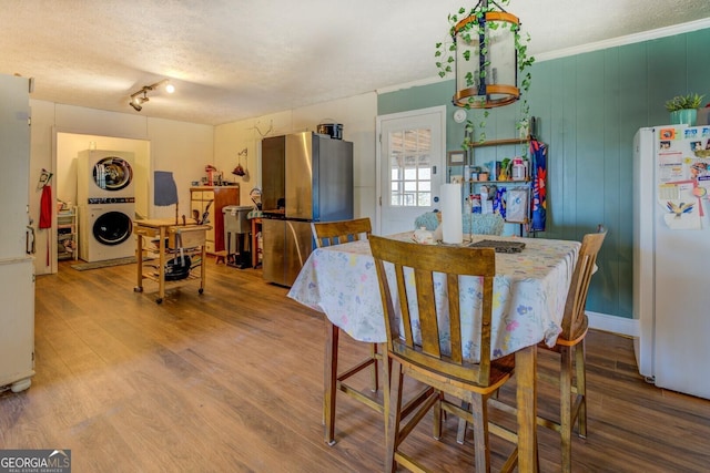 dining area featuring stacked washer and clothes dryer, crown molding, a textured ceiling, and wood finished floors