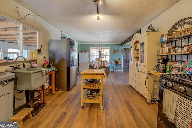 kitchen with open shelves, a sink, a textured ceiling, wood finished floors, and white appliances