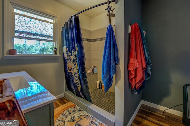 full bath with a stall shower, wood finished floors, vanity, and baseboards