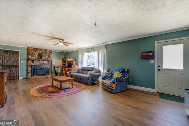 living room featuring ornamental molding, a textured ceiling, baseboards, and wood finished floors