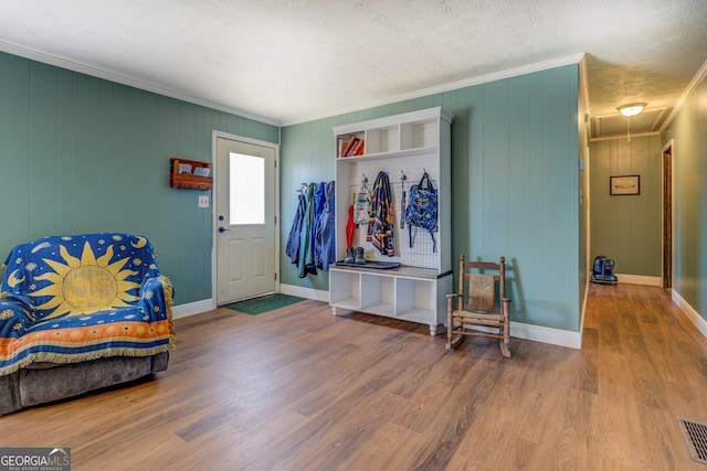 mudroom with attic access, a textured ceiling, ornamental molding, and wood finished floors